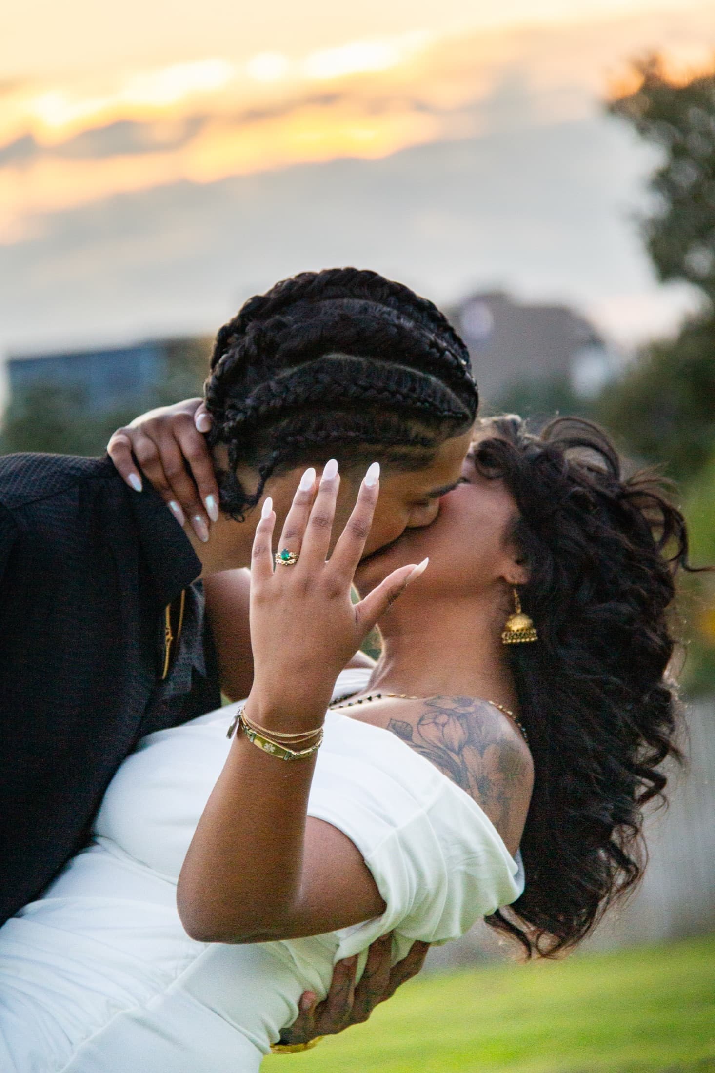 Dash and Robyn kissing at sunset, Robyn's hand raised over his shoulder showing her emerald engagement ring