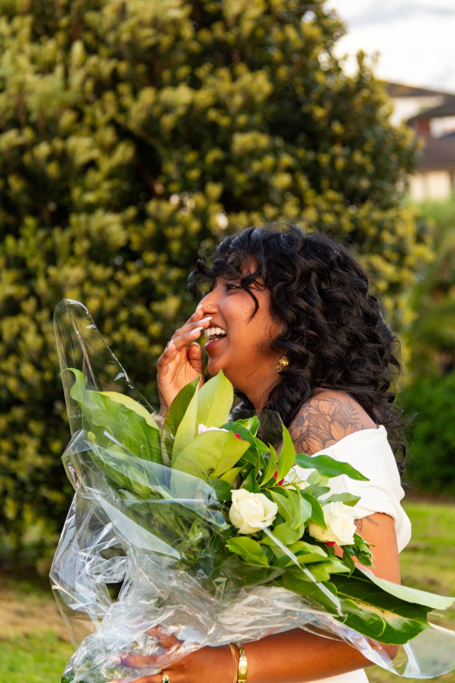 Robyn laughing while holding a wrapped bouquet of white roses in the evening light