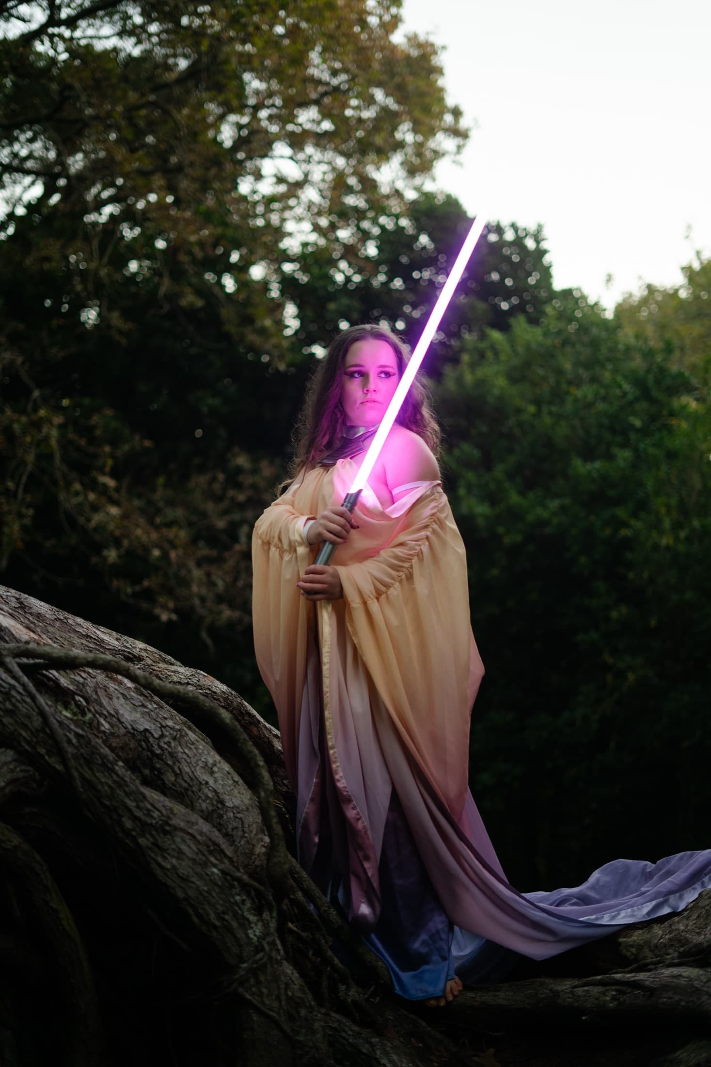 Model raising a lit lightsaber overhead amid dense green foliage