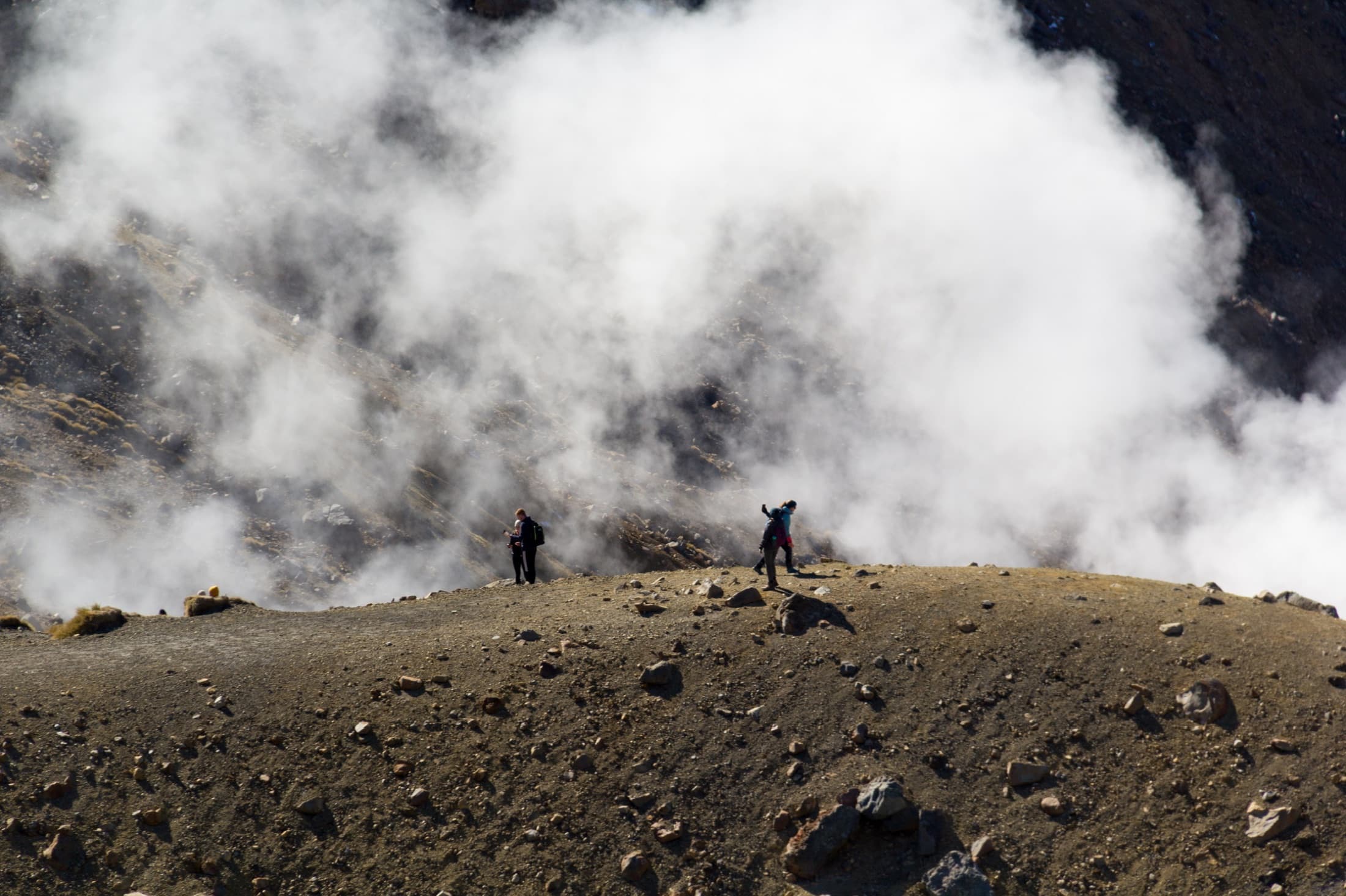 Two hikers on a ridge silhouetted against billowing volcanic steam